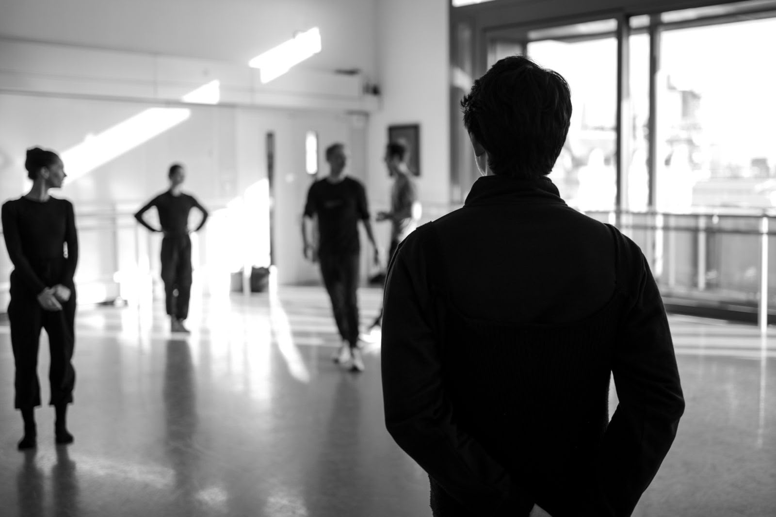 A black-and-white view across a ballet class from behind the teacher